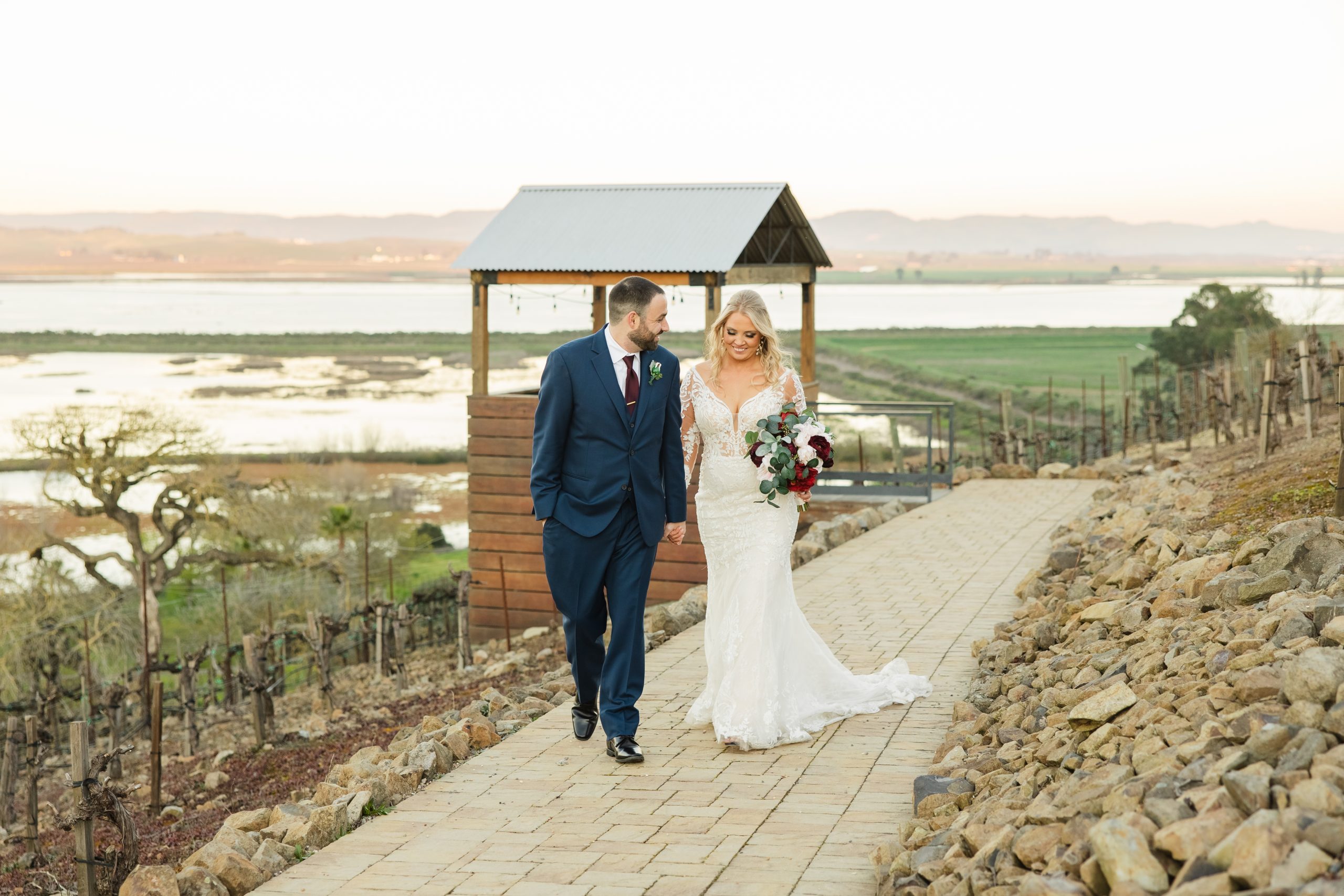 A bride and groom walking on an outdoor path in a wine country wedding.