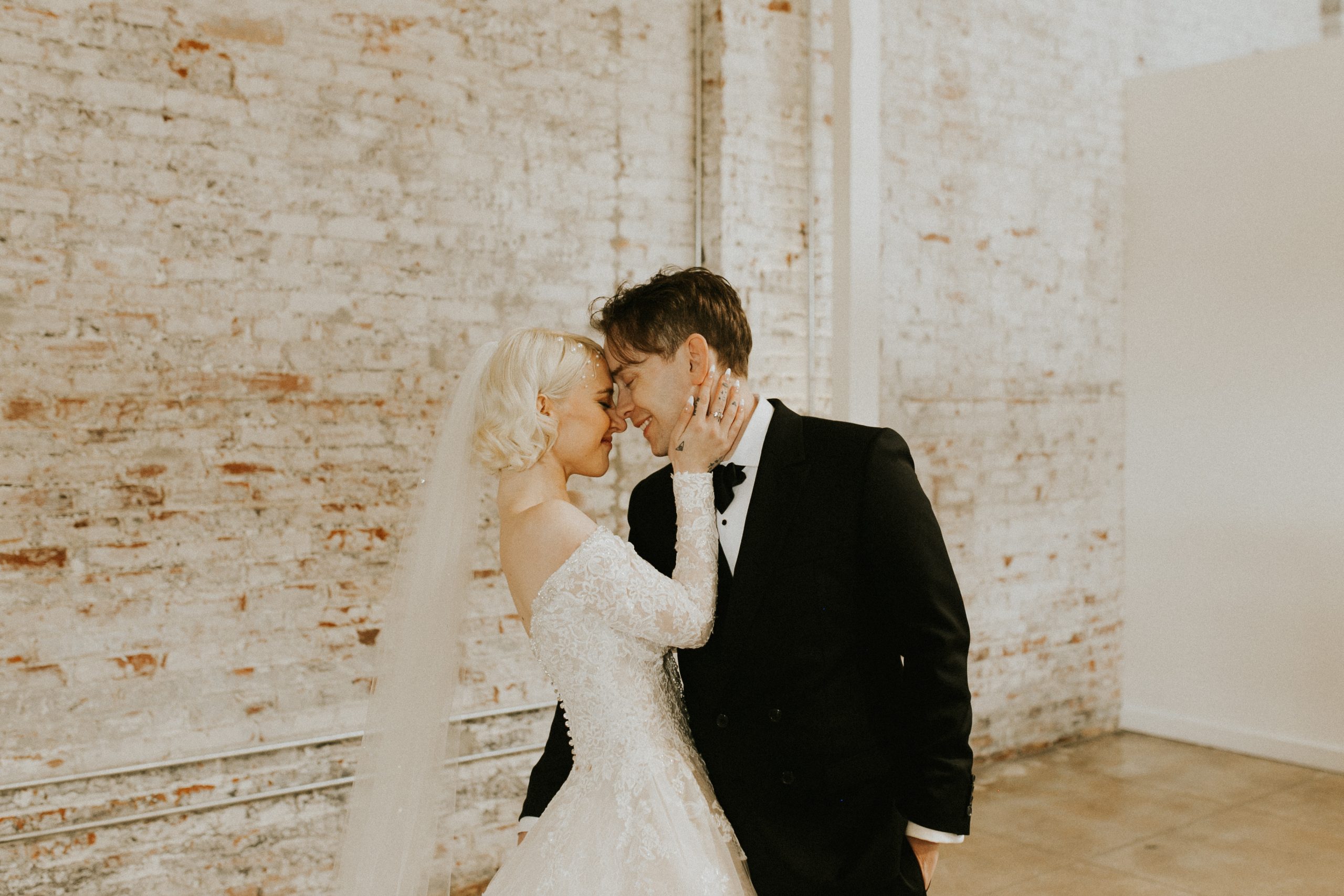 A happy bride and groom against a whitewashed brick wall.